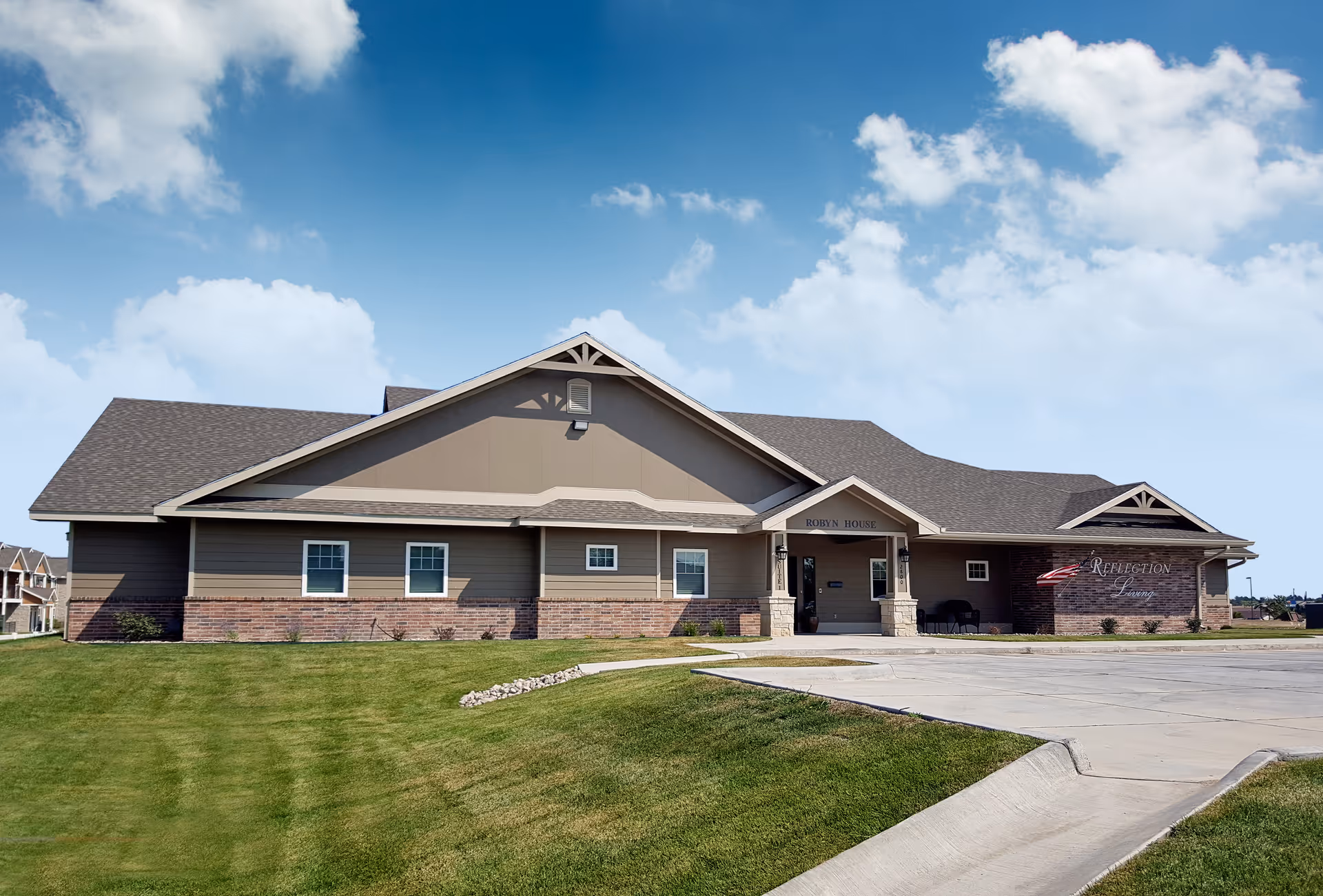 Front exterior of a single-story senior living facility building with a green lawn under a blue sky.