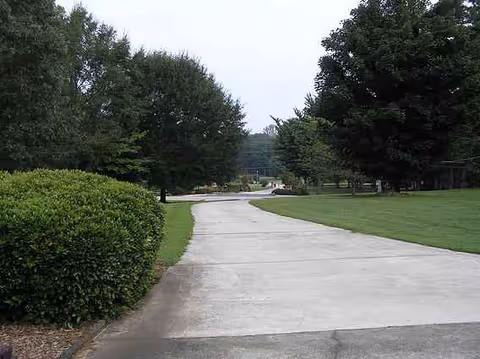 Pathway winds through a grassy campus with trees and shrubs at a senior care facility.