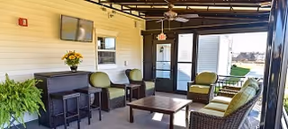 Covered outdoor patio with wicker seating, a coffee table, a bar counter with stools, a wall-mounted TV and ceiling fans.