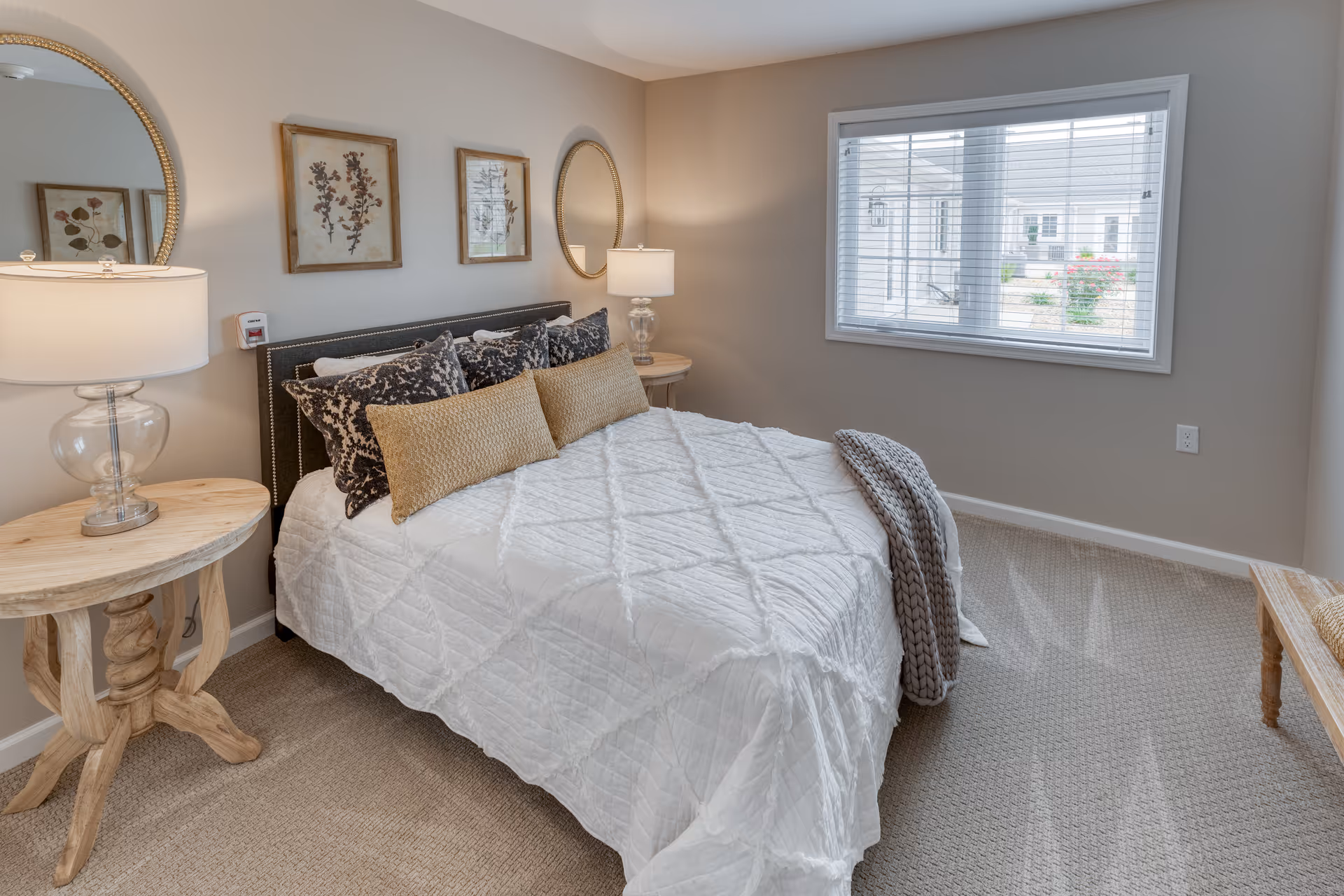Bright, neatly staged bedroom with a made bed, bedside tables and lamps, wall art and a window.