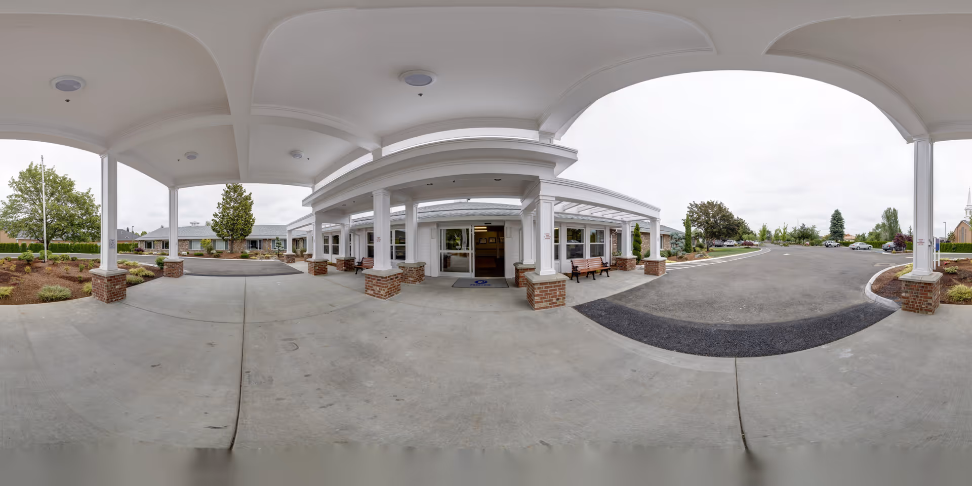 Covered porte-cochère entrance and driveway of a post-acute care building with columns, benches, and landscaped grounds.