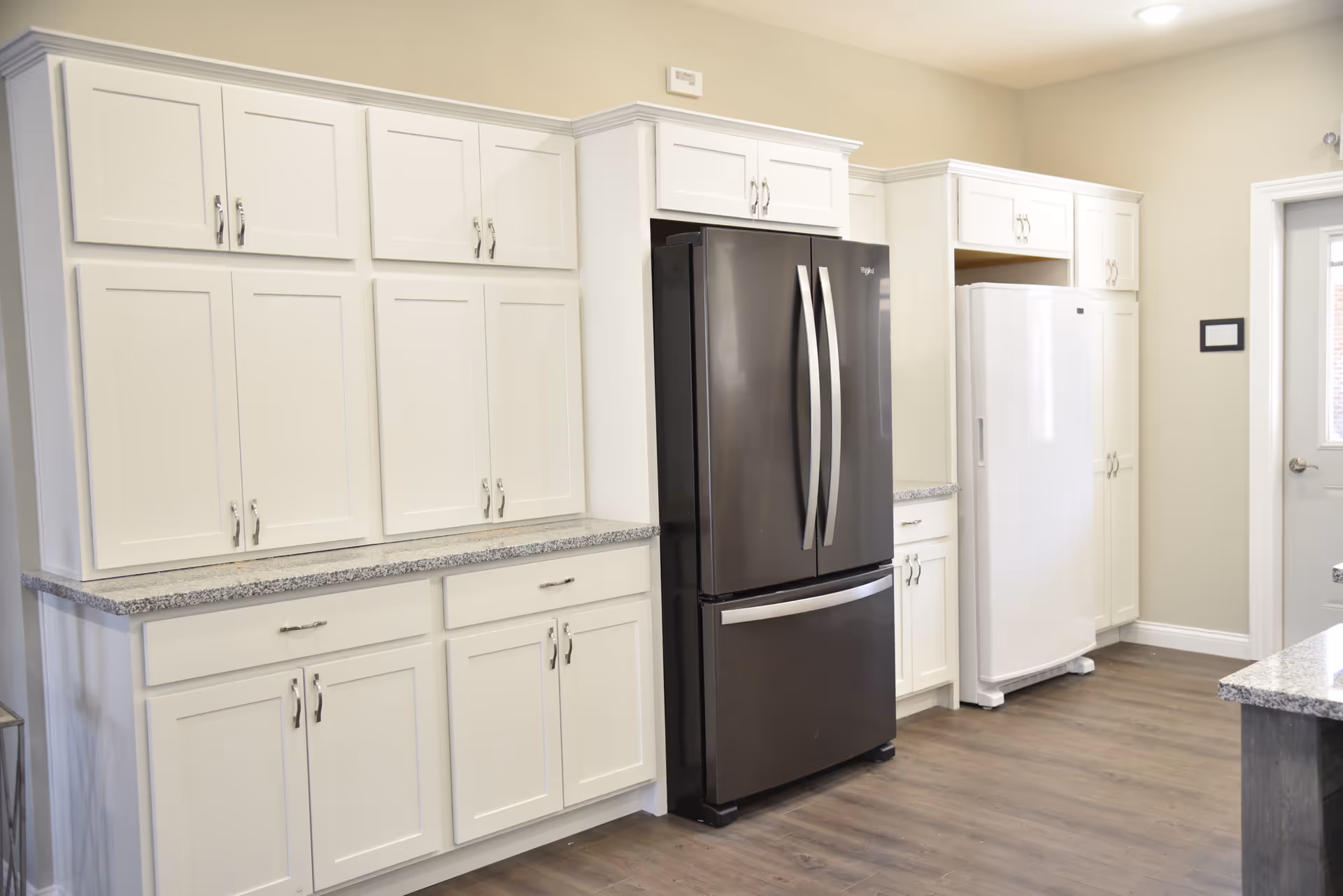 Bright modern kitchen with white cabinetry, granite countertops, a stainless-steel French-door refrigerator and a white upright freezer.
