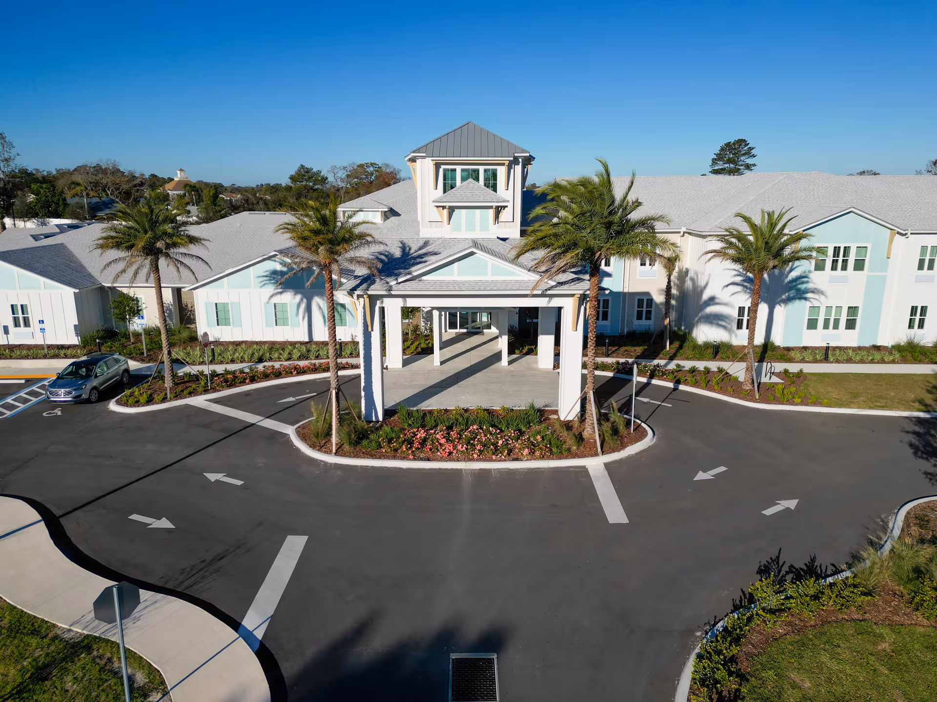 Front entrance of a coastal-style senior living building with a covered porte-cochere, palm trees, and a circular driveway.