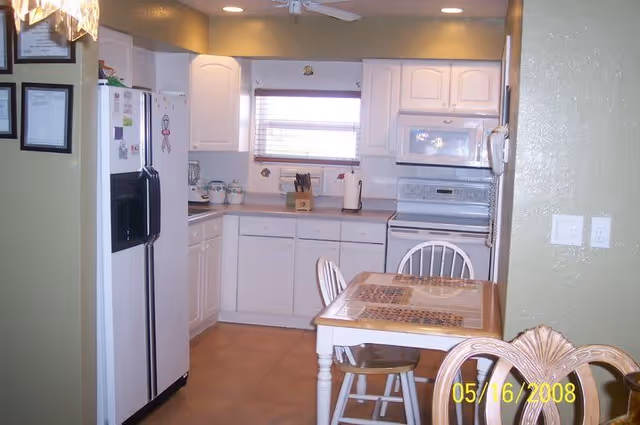Small kitchen with white cabinets, refrigerator, stove, and a dining table with chairs in the foreground.