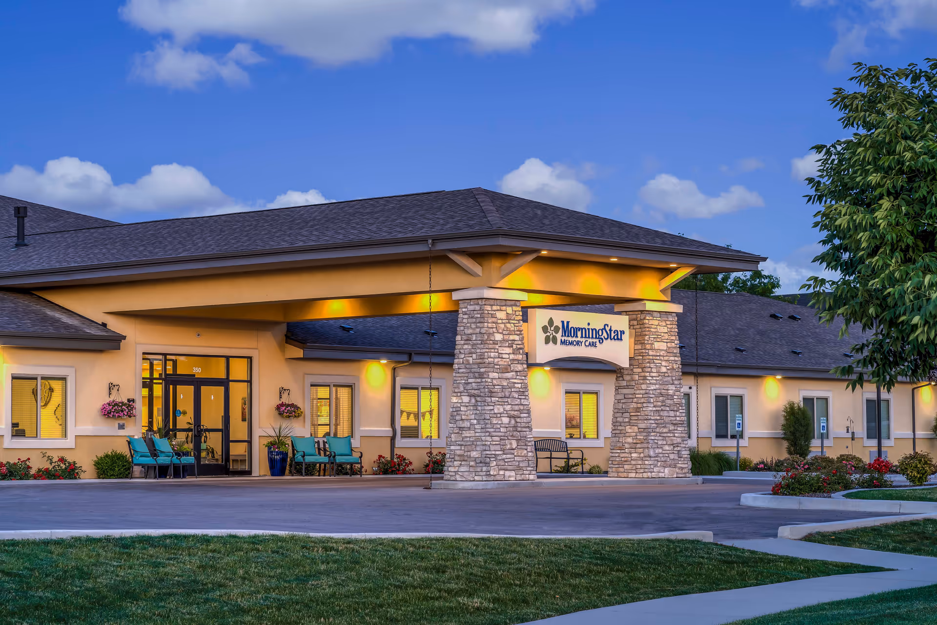 Exterior front entrance of a memory care facility with a covered driveway, stone pillars, and an illuminated "MorningStar Memory Care" sign.