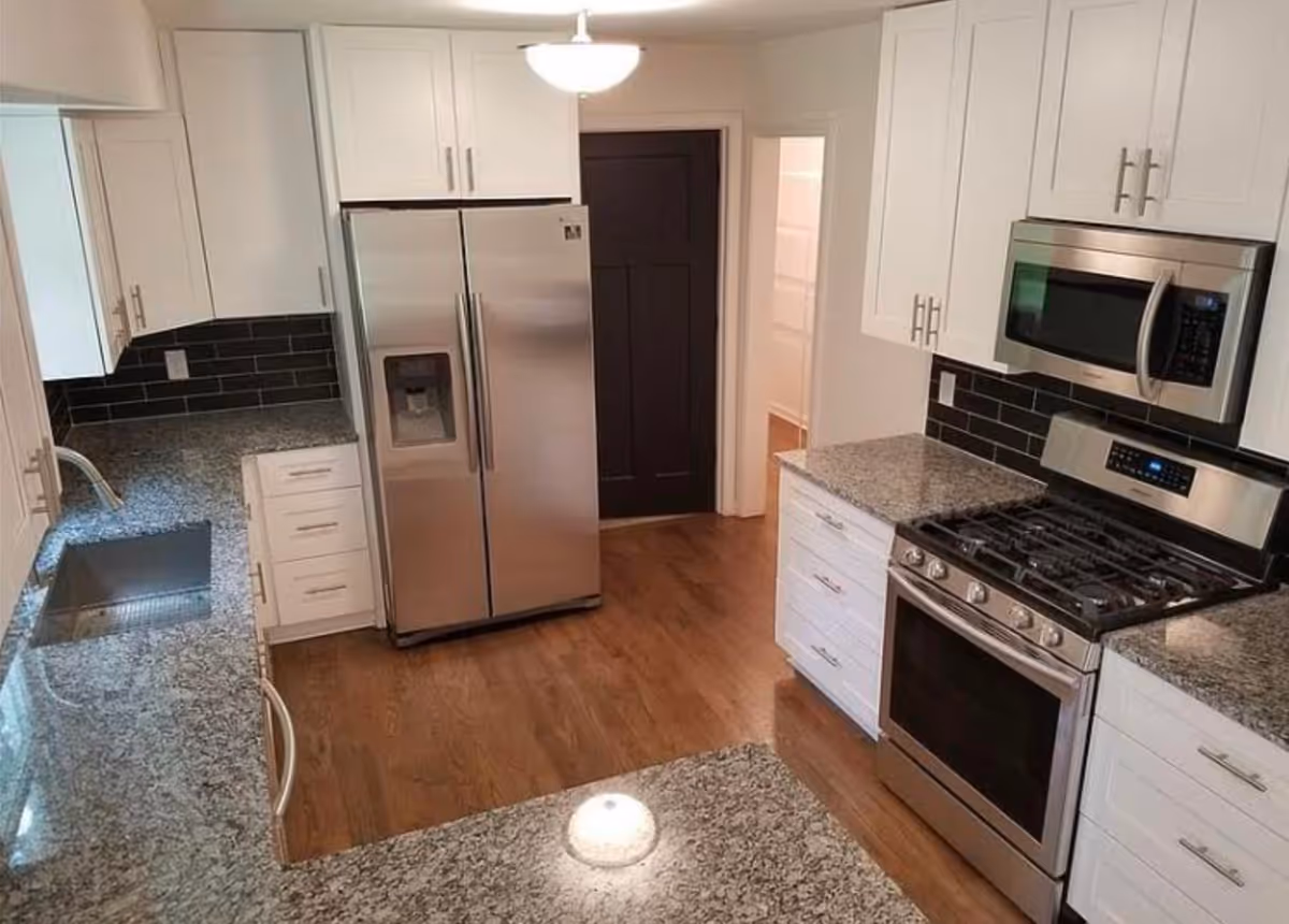 Modern kitchen with stainless steel refrigerator, gas range and microwave, white cabinets, and granite countertops.