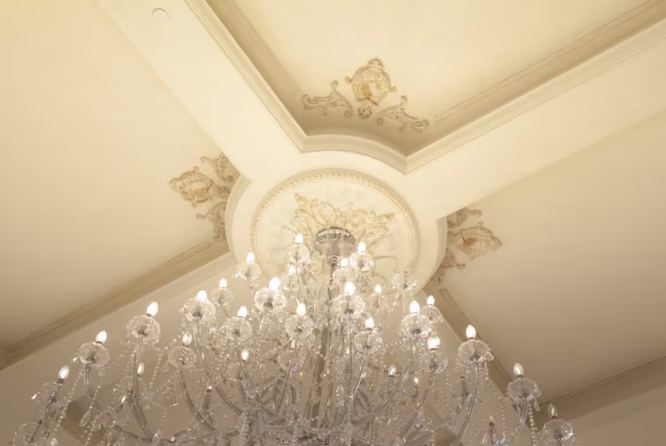 Ornate ceiling with decorative molding and a large crystal chandelier with multiple lit bulbs hanging from the center.