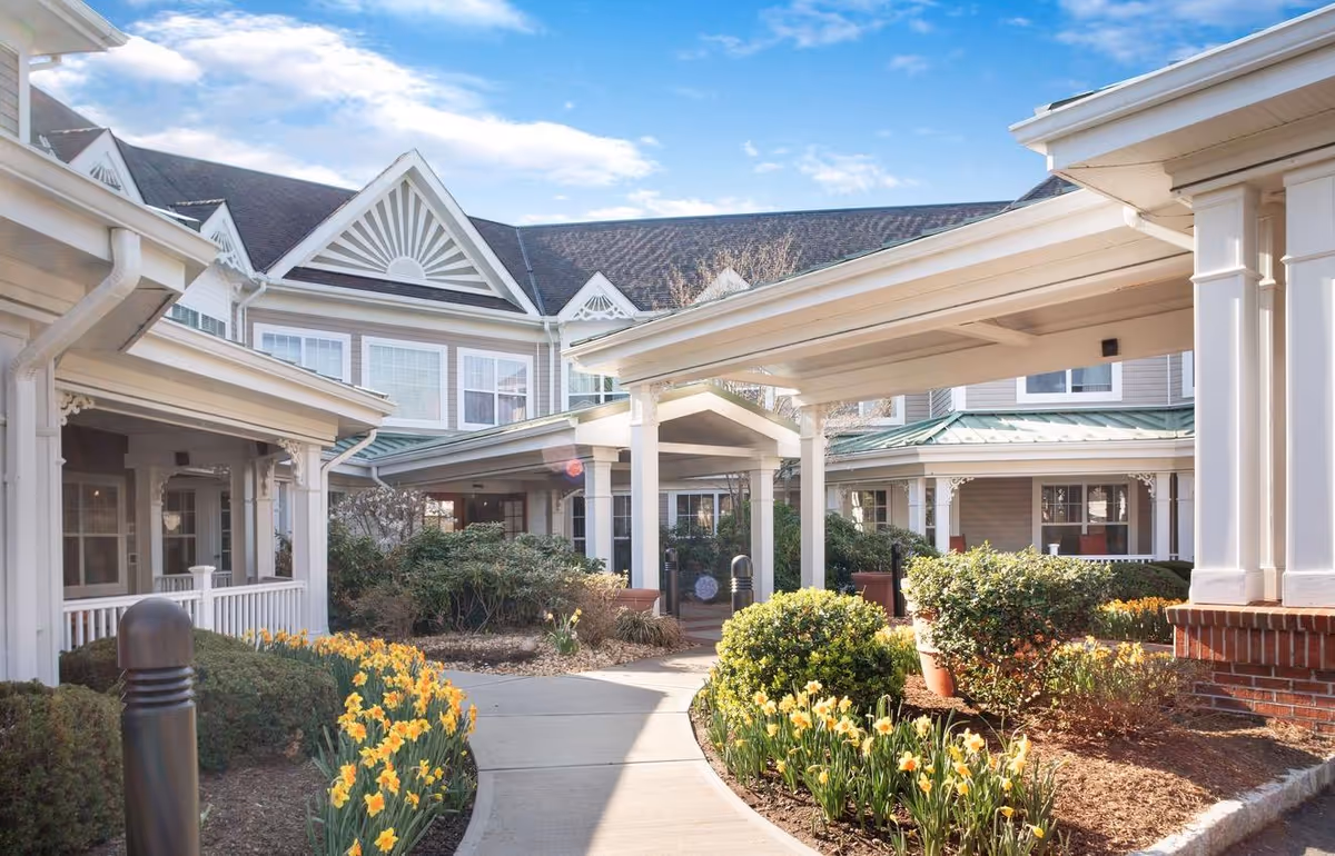 Front entrance of a senior living building with covered walkways, landscaped beds and blooming yellow daffodils.