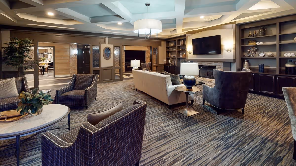 Spacious communal living room with sofas and armchairs arranged around a coffee table, built-in shelving, a wall-mounted TV and ambient lighting.