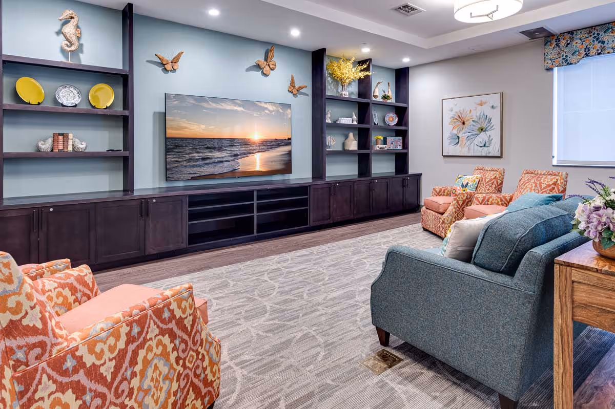 Cozy common room with upholstered chairs and a sofa facing a wall-mounted TV and built-in shelving.
