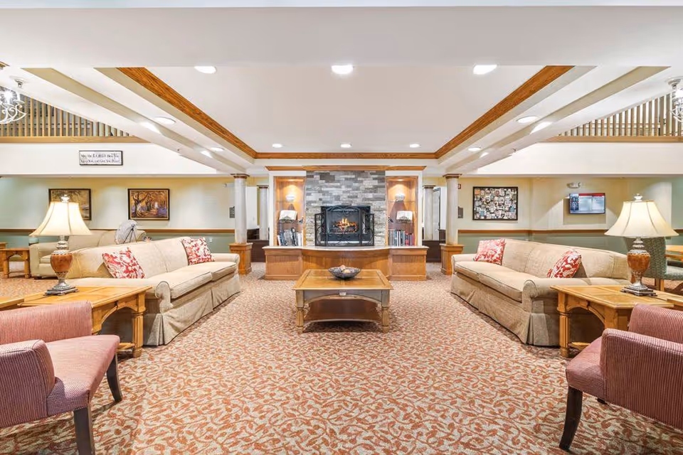 Spacious senior living lounge with sofas, armchairs, a coffee table, and a central stone fireplace.