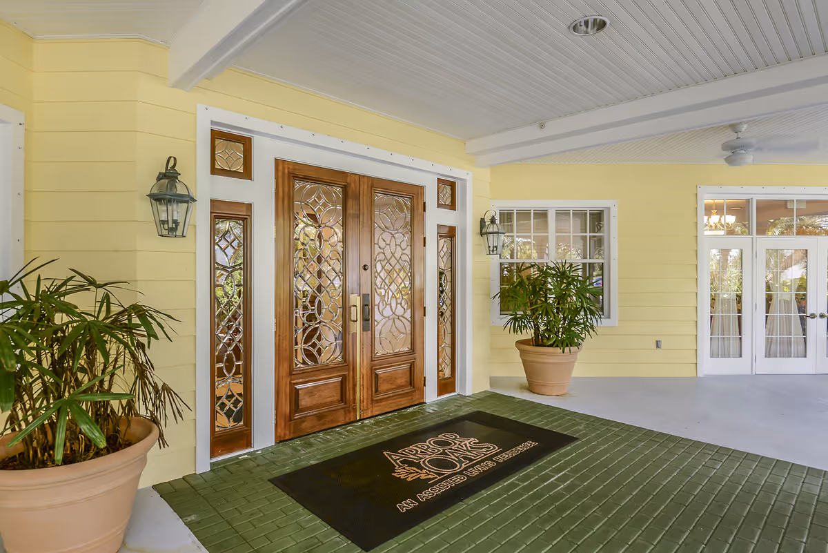 Covered entrance with decorative double wooden doors, potted plants, and a welcome mat reading 'Arbor Oaks'.