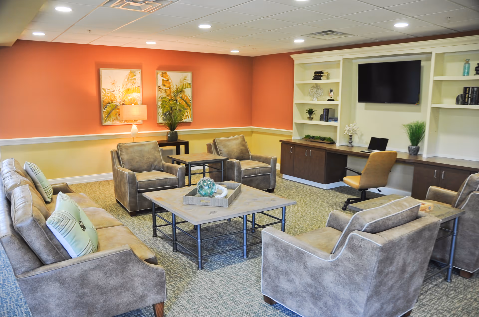 Comfortable lounge with sofas and armchairs arranged around a coffee table, built-in shelving and a wall-mounted TV.