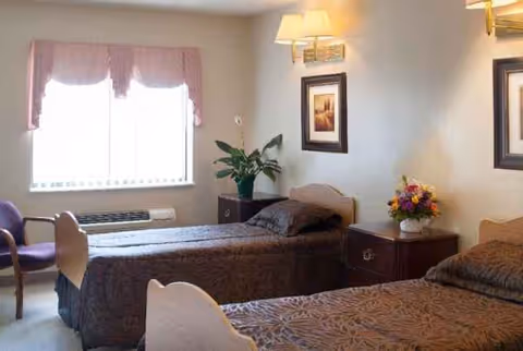 Two single beds in a warmly lit bedroom with plants, bedside tables, and a window.