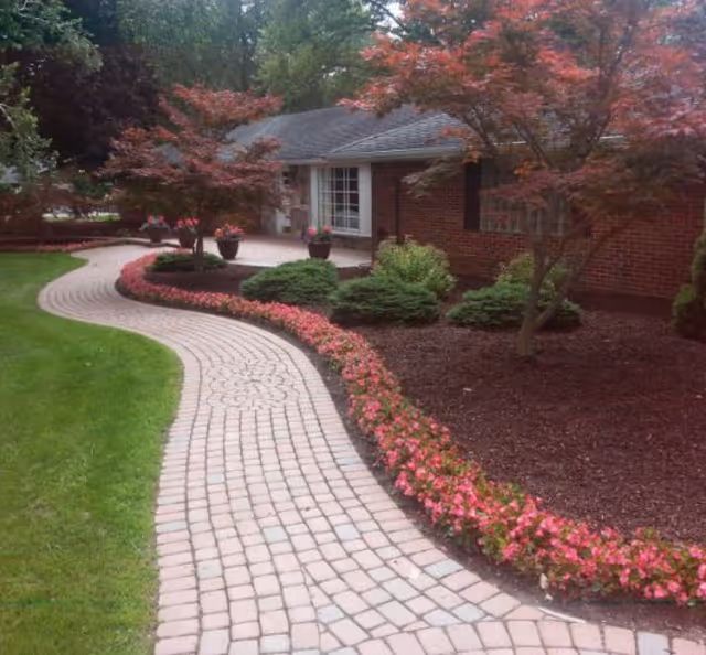 Front of Fairlane Assisted Living LLC entrance with curved brick walkway and blooming landscaping.