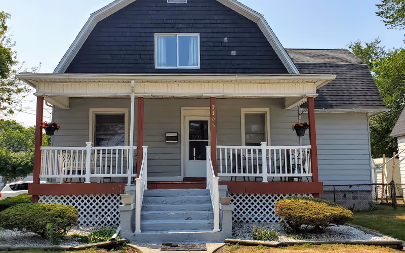 Front view of a small, two-story house with a welcoming porch and white railings.
