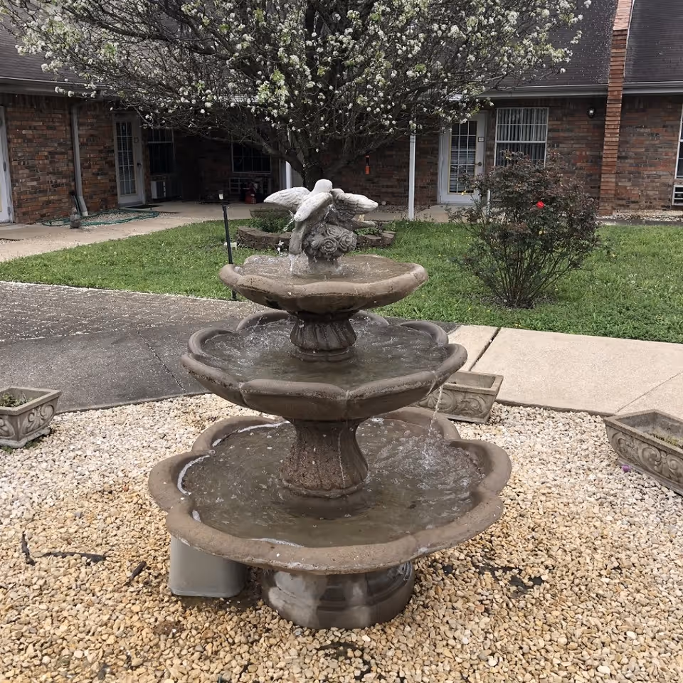 Stone-tier fountain in a brick courtyard with a blooming tree and shrubs.