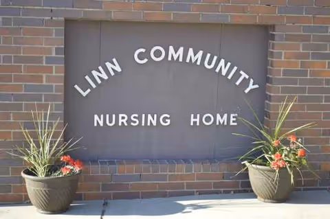 Exterior brick wall with Linn Community Nursing Home sign and two potted plants.
