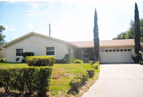 A single-story senior living facility with a front yard, driveway, and trimmed hedges.