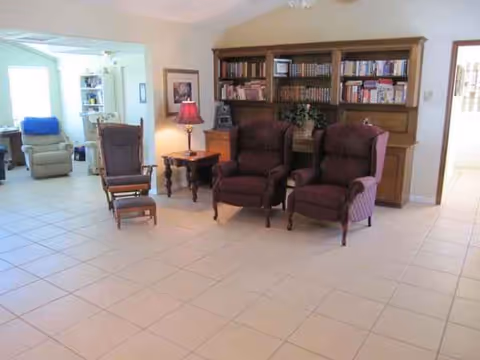 A spacious living room with burgundy chairs, a wooden cabinet, and a tiled floor.