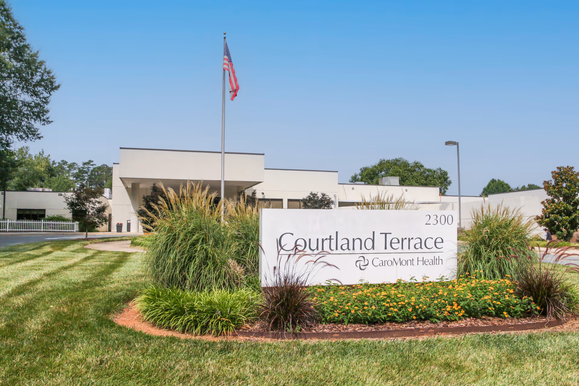 Front exterior of Courtland Terrace facility with landscaped sign, lawn, and an American flag in front of the building.