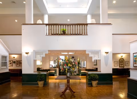 Spacious two-story lobby with a central floral arrangement, balcony, columns, and seating areas.