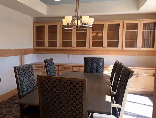 Dining room with a rectangular table, upholstered chairs, an overhead chandelier, and built-in wooden cabinets with glass doors.