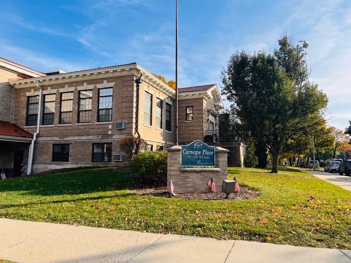 Front exterior of Carnegie Place, a brick building with its entrance sign on the lawn and small American flags.