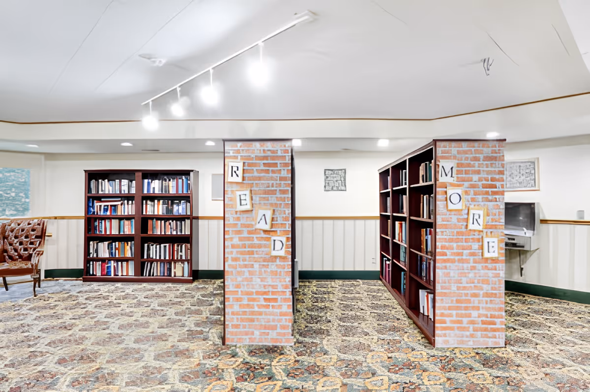 Well-lit interior reading room with bookshelves flanking brick pillars decorated with the letters 'READ' and 'MORE'.