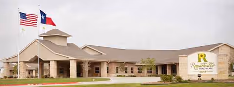 Exterior view of a single-story senior living facility with flags and a prominent entrance sign.