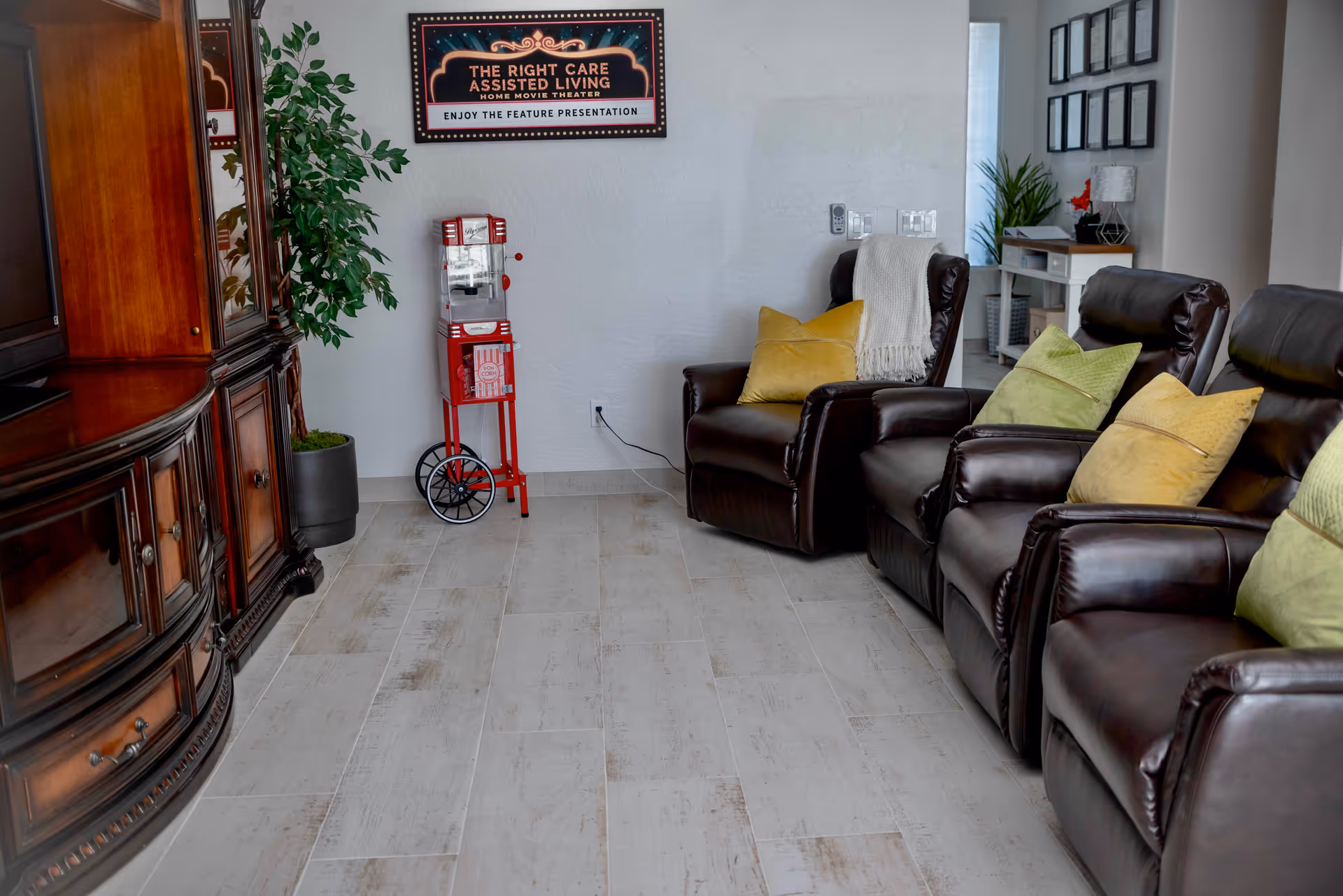 A home-theater style lounge with three brown leather recliners with colorful pillows, a popcorn machine, and a wooden entertainment cabinet.