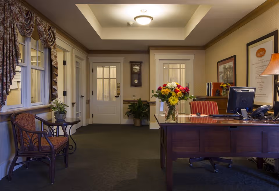 Warmly lit reception area with a wooden desk, computer, vase of flowers, seating chairs and double doors.