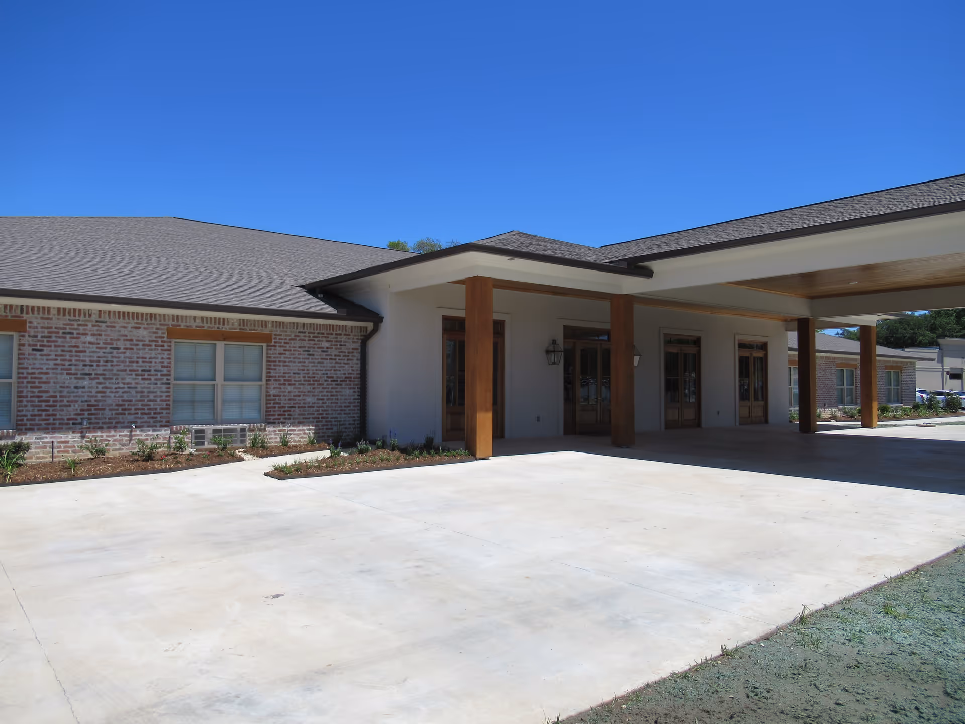 Exterior view of a single-story brick building with a covered entrance supported by wooden pillars under a clear blue sky.
