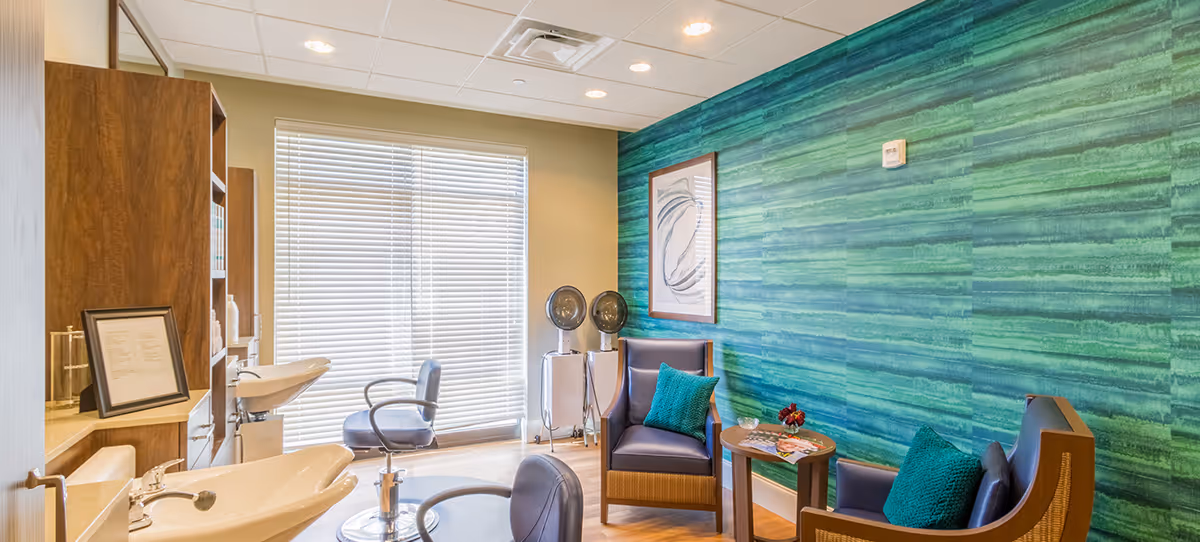 Bright salon-style interior with hair-washing sinks, styling chairs and a small seating area against a green accent wall.