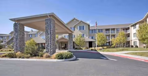 Brick-and-stone senior living facility exterior with entrance canopy and flag.