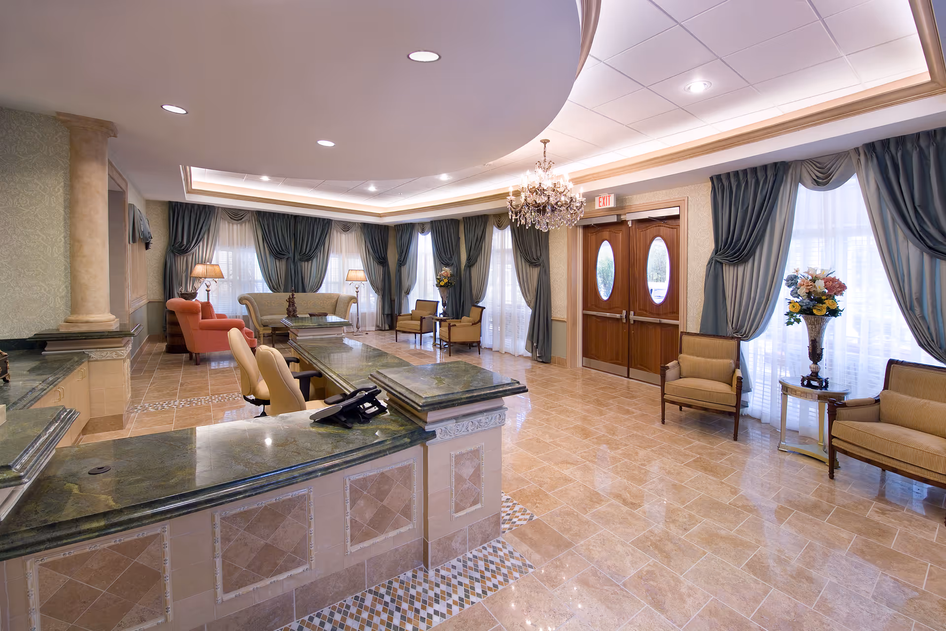 Spacious and elegant reception area with a curved green marble countertop desk, beige tiled floor, chandelier, large windows with blue drapes, and various seating including armchairs and sofas.