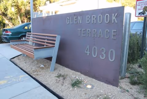 Outdoor sign reading Glen Brook Terrace 4030 with a wooden bench nearby.