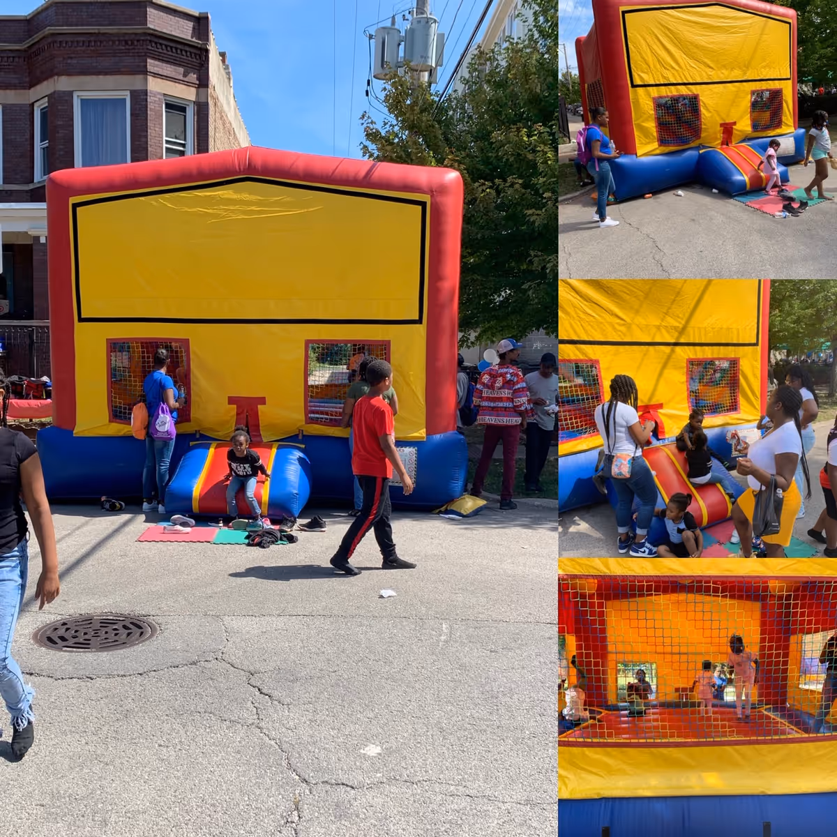 A large yellow and red inflatable bounce house set up outdoors on a street with children playing inside and around it. Several adults and children are standing nearby, some watching and some interacting with the kids. The background shows a brick building and trees under a clear blue sky.