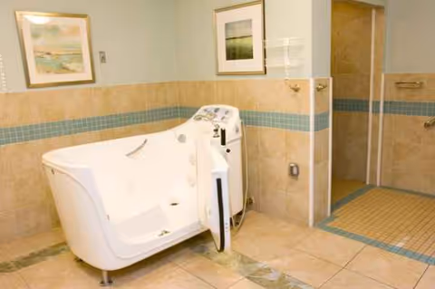 Accessible white bathtub with controls in a tiled bathroom with wall art.