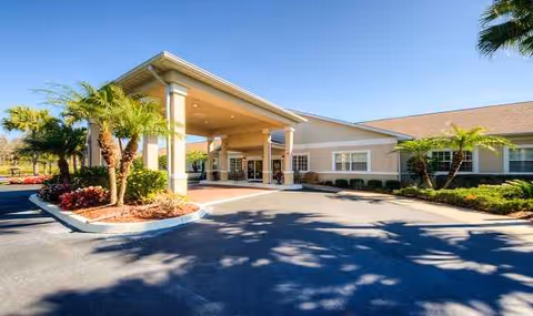 Senior living facility entrance with a covered drive, columns, and landscaped palm trees.