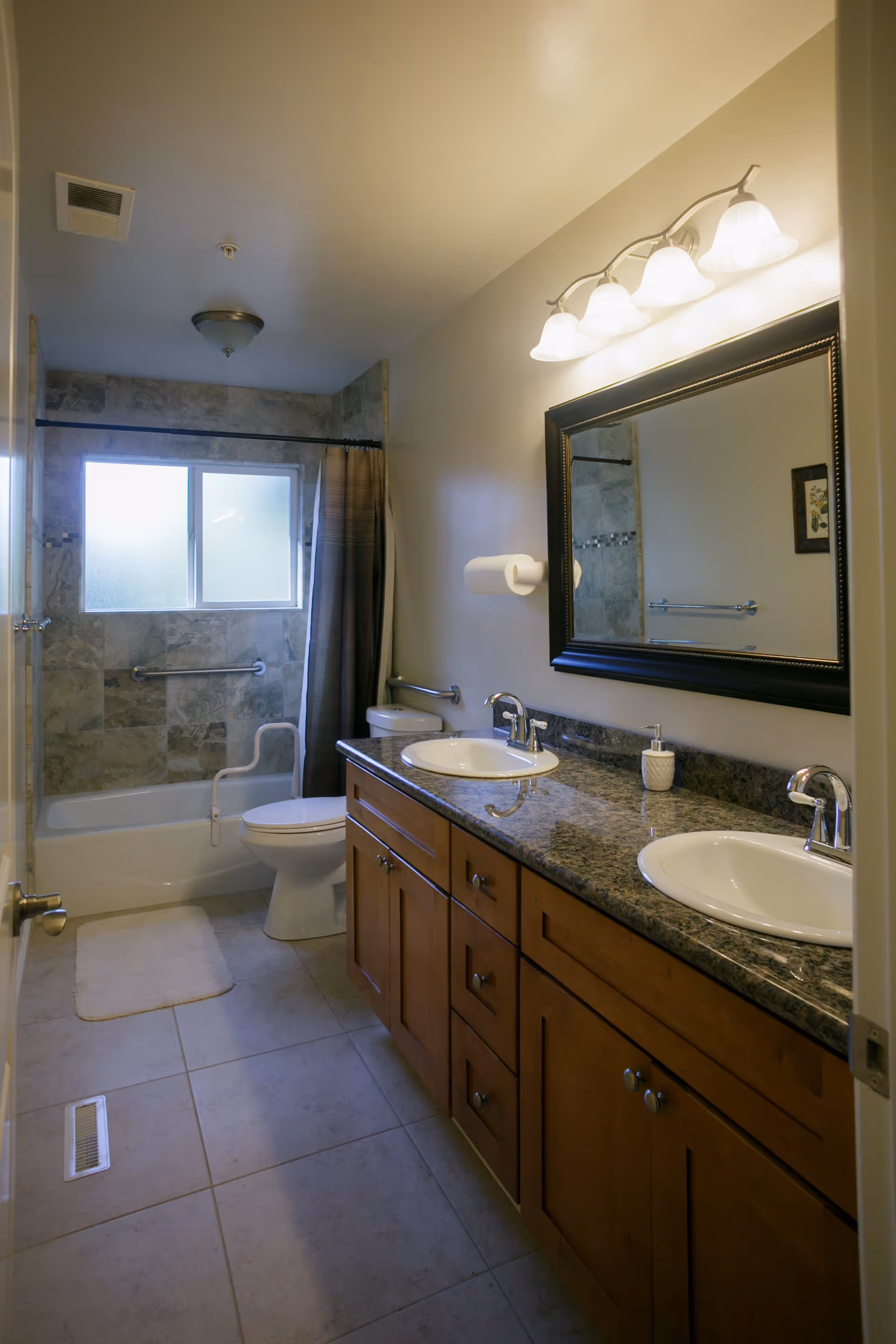 Bathroom featuring a double-sink granite vanity, large mirror, toilet, and a bathtub/shower with grab bars.