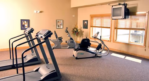 Exercise room with treadmills, stationary and recumbent bikes, windows with blinds, and a ceiling-mounted TV.