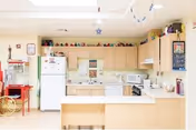 Bright senior living facility kitchen with white appliances and light wood cabinets.