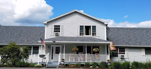 Front exterior of a white two-story house with a covered porch, potted plants, and an American flag.