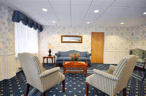 Common living room with blue sofa, patterned chairs, coffee table, lamps, and floral wallpaper.