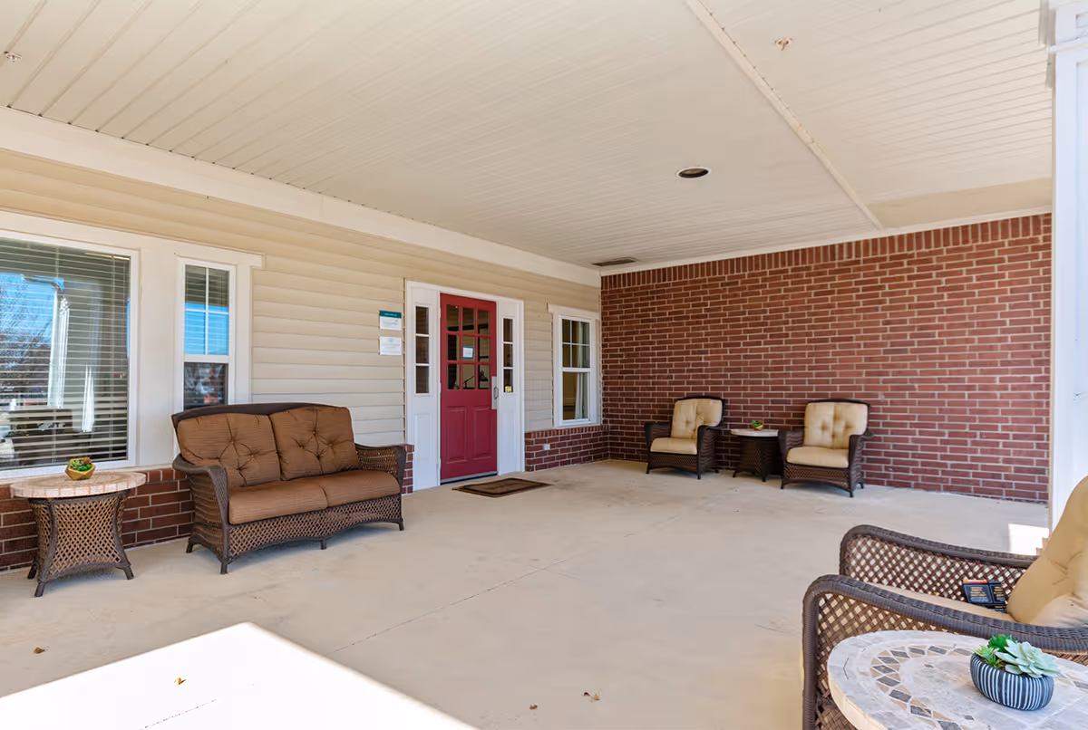 Covered entrance patio with wicker seating and a red front door.