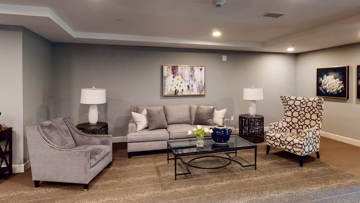 Contemporary living room with a gray sofa, two armchairs, glass coffee table and wall art.