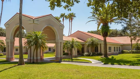 Exterior view of Crescent Health & Rehabilitation Center featuring a single-story building with a red-tiled roof, arched entrance, palm trees, and well-maintained green lawn under a clear blue sky.