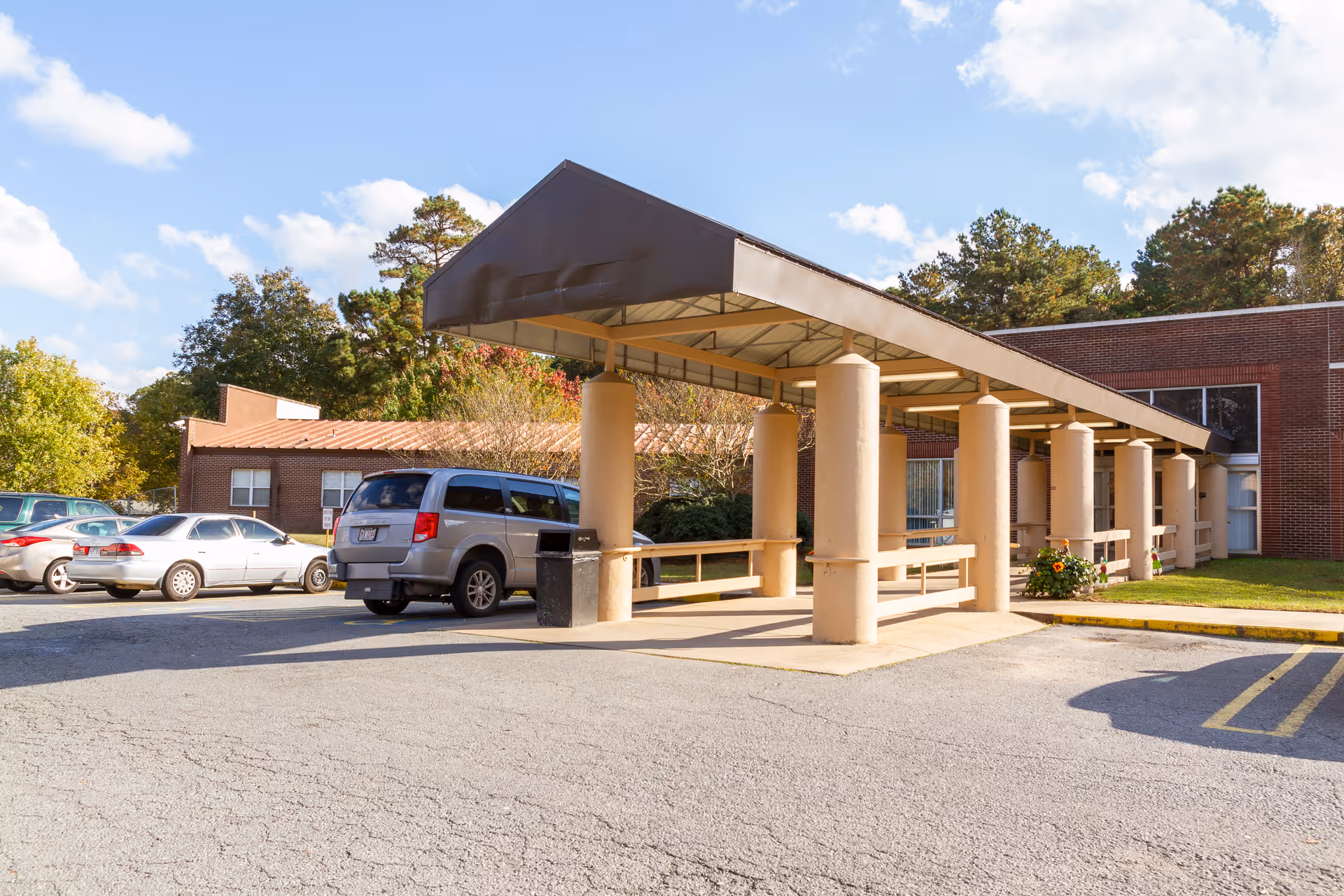 Covered entrance canopy and drive-up drop-off area in front of a brick senior living building with parked cars.