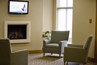 A seating area with upholstered armchairs arranged around a fireplace and a wall-mounted TV beside a tall window.